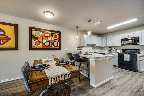 a open kitchen with stainless steel appliances granite countertop a stove top oven a sink a dining table and chairs with wooden floor