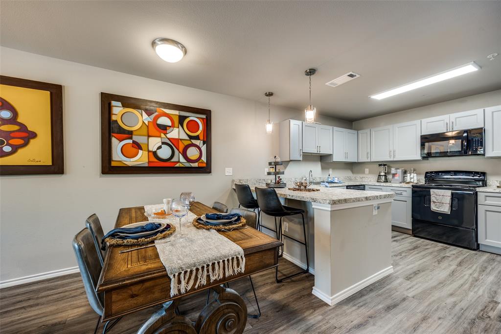 6108 Abrams Road, Unit 205 Dallas, TX 75231 - Photo 6 of 12 Kitchen featuring black appliances, a kitchen breakfast bar, a peninsula, light wood-type flooring, and hanging light fixtures