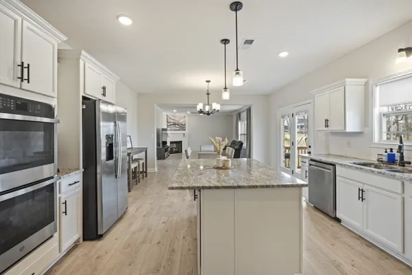 a kitchen with stainless steel appliances granite countertop a refrigerator a sink dishwasher a oven and white cabinets with wooden floor