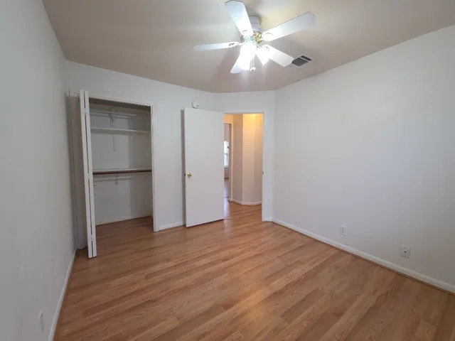 an empty room with wooden floor and a ceiling fan