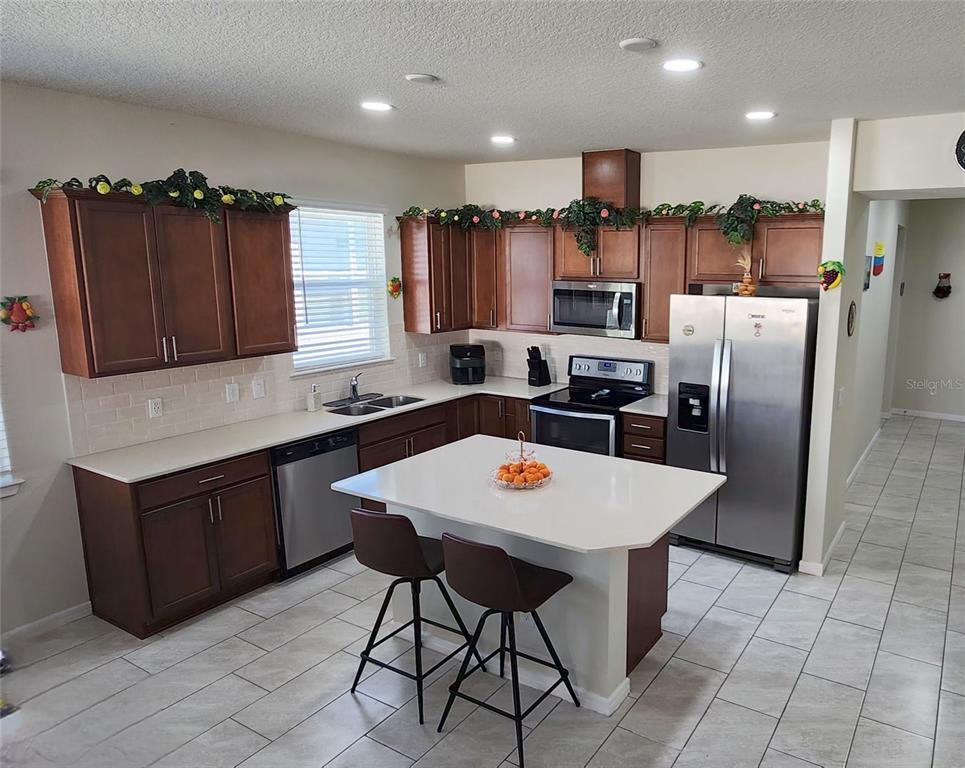 1823 Spring Shower Circle Kissimmee, FL 34744 - Photo 5 of 38 a kitchen with stainless steel appliances granite countertop a table chairs sink refrigerator and microwave