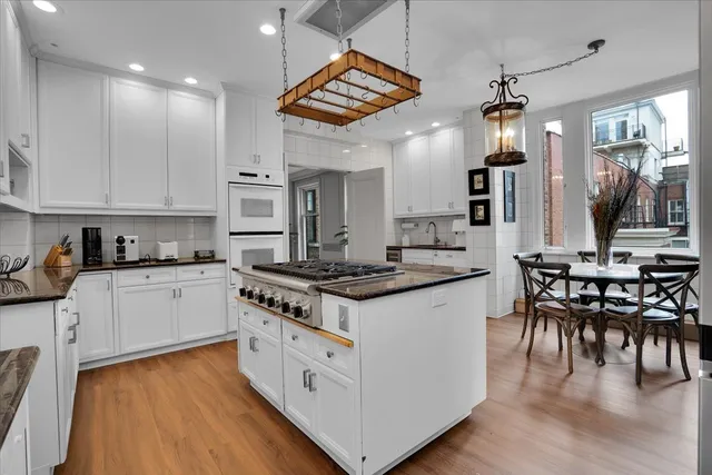 a kitchen with stainless steel appliances granite countertop wooden cabinets a sink a stove a dining table and chairs