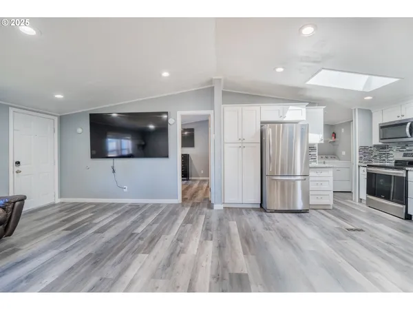 a view of empty room with wooden floor and kitchen view
