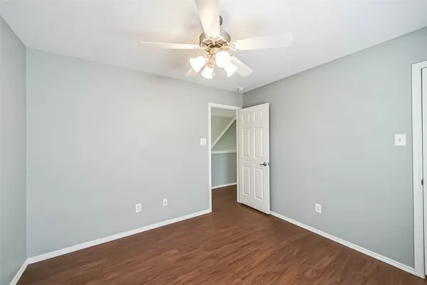 a view of an empty room with wooden floor and a ceiling fan
