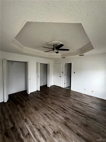a view of an empty room with wooden floor and a ceiling fan