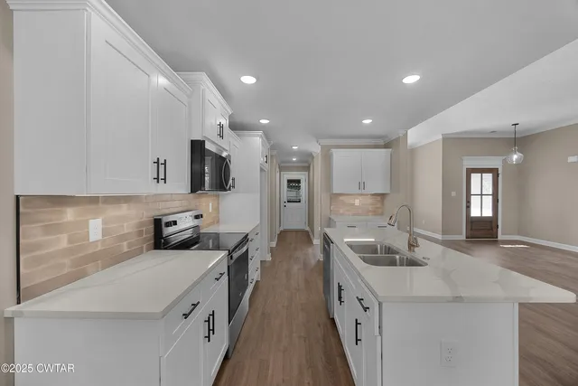 a large white kitchen with stainless steel appliances kitchen island a stove a sink a refrigerator and a cabinets