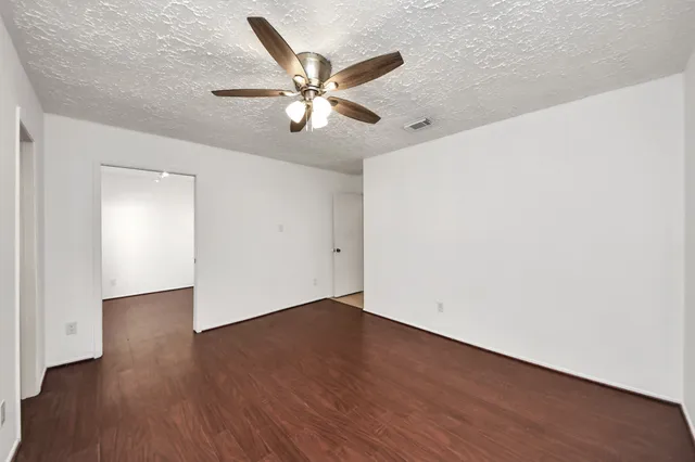 an empty room with wooden floor fan and windows