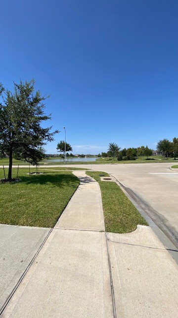 5002 Naples Grove Lane Rosharon, TX 77583 - Photo 37 of 38 Charming neighborhood with well-maintained sidewalks, lush green lawns, and a serene view of the nearby water feature under a clear blue sky.