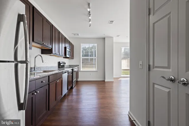 a kitchen with stainless steel appliances granite countertop a refrigerator a sink dishwasher a stove and white countertops with wooden floor