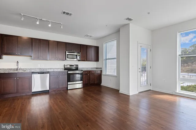 a kitchen with granite countertop wooden floors stainless steel appliances and sink