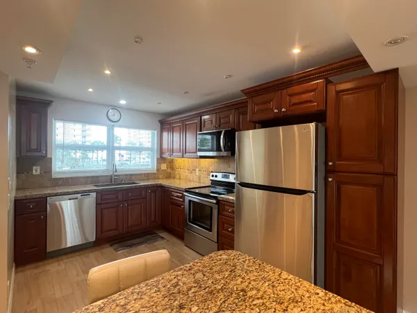 a kitchen with stainless steel appliances granite countertop a refrigerator a sink dishwasher a stove with white cabinets and wooden floor