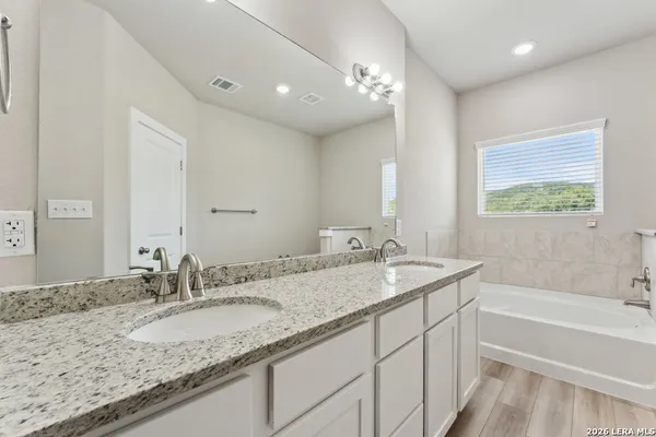 a bathroom with a granite countertop double vanity sink and mirror with bathtub