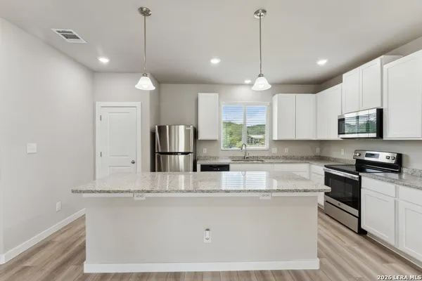 a large kitchen with granite countertop a stove a sink a center island and cabinets