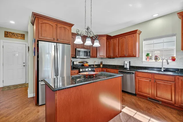 a kitchen with stainless steel appliances granite countertop a refrigerator a sink dishwasher a stove with wooden cabinets and floor