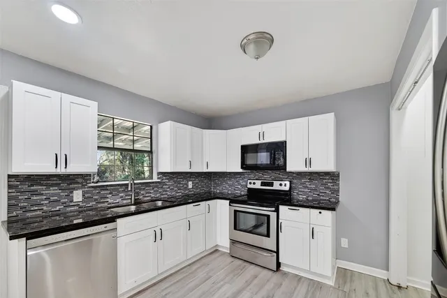a kitchen with granite countertop white cabinets white appliances a sink and a window