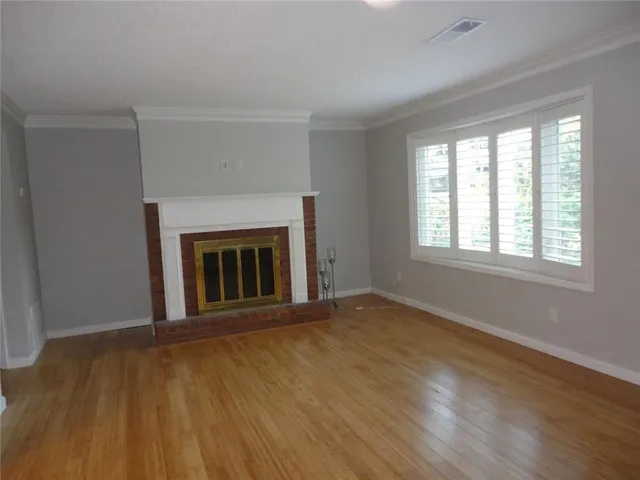 a view of an empty room with wooden floor fireplace and a window
