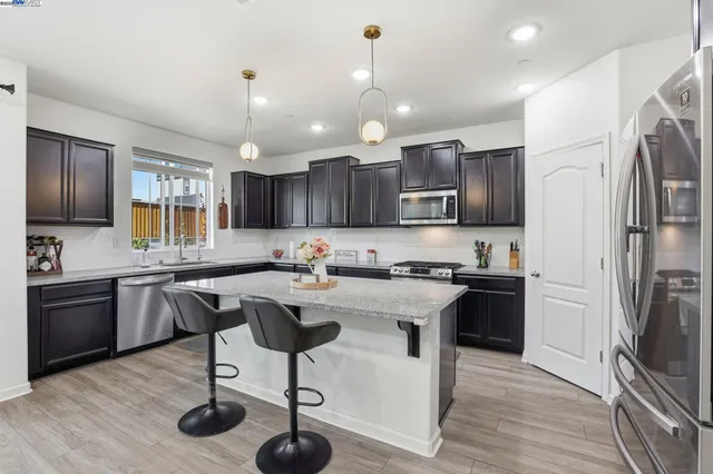 a kitchen with stainless steel appliances granite countertop a refrigerator a stove top oven a sink dishwasher a dining table and chairs with wooden floor