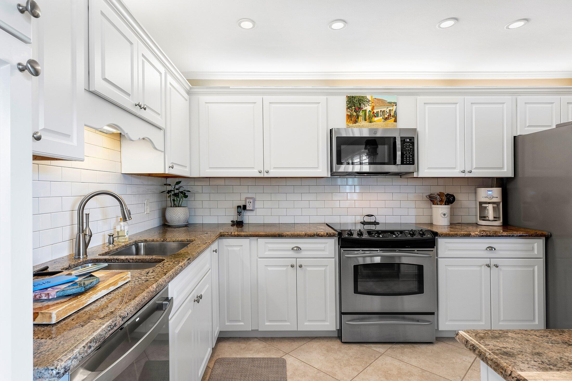 10093 Quail Covey Road, Unit HIBISCUS N Boynton Beach, FL 33436 - Photo 8 of 34 a kitchen with stainless steel appliances granite countertop a stove and white cabinets