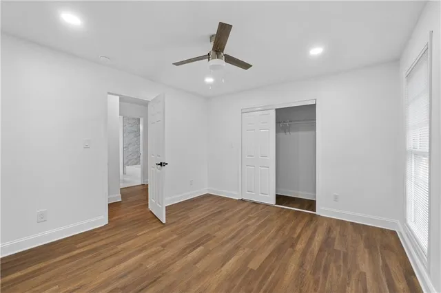 an empty room with wooden floor ceiling fan and windows
