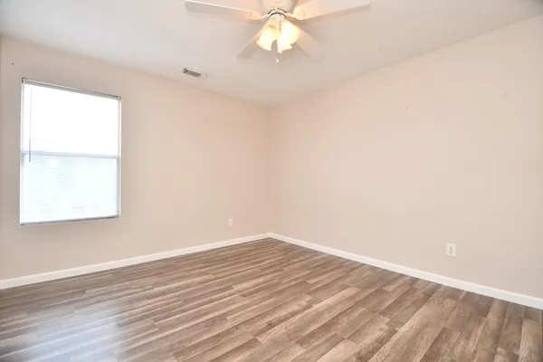 an empty room with wooden floor fan and windows