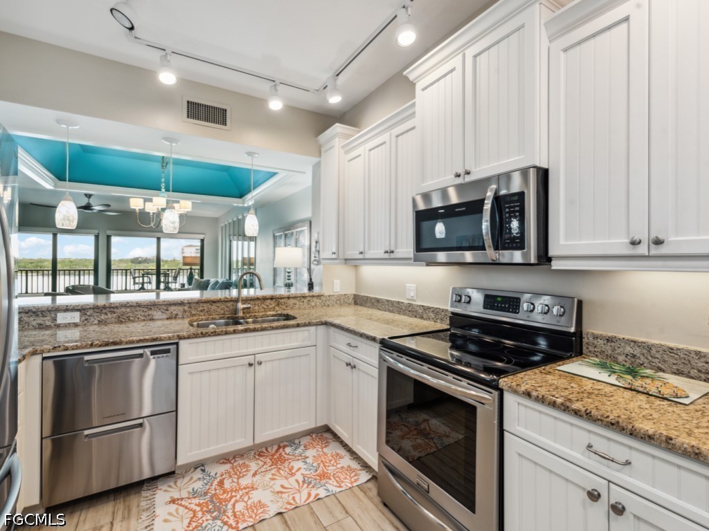 232 La Peninsula Boulevard, Unit 232 Naples, FL 34113 - Photo 6 of 44 a kitchen with granite countertop a sink stainless steel appliances and white cabinets