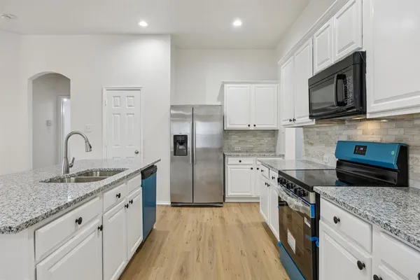 a large kitchen with granite countertop a stove top oven a sink dishwasher and white cabinets with wooden floor