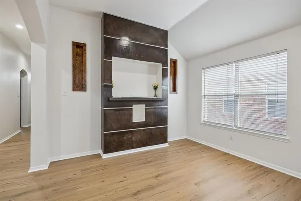 a view of an empty room and kitchen with wooden floor