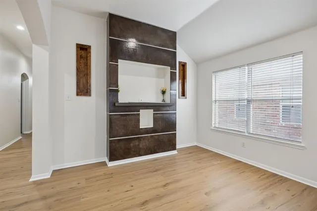 a view of an empty room and kitchen with wooden floor