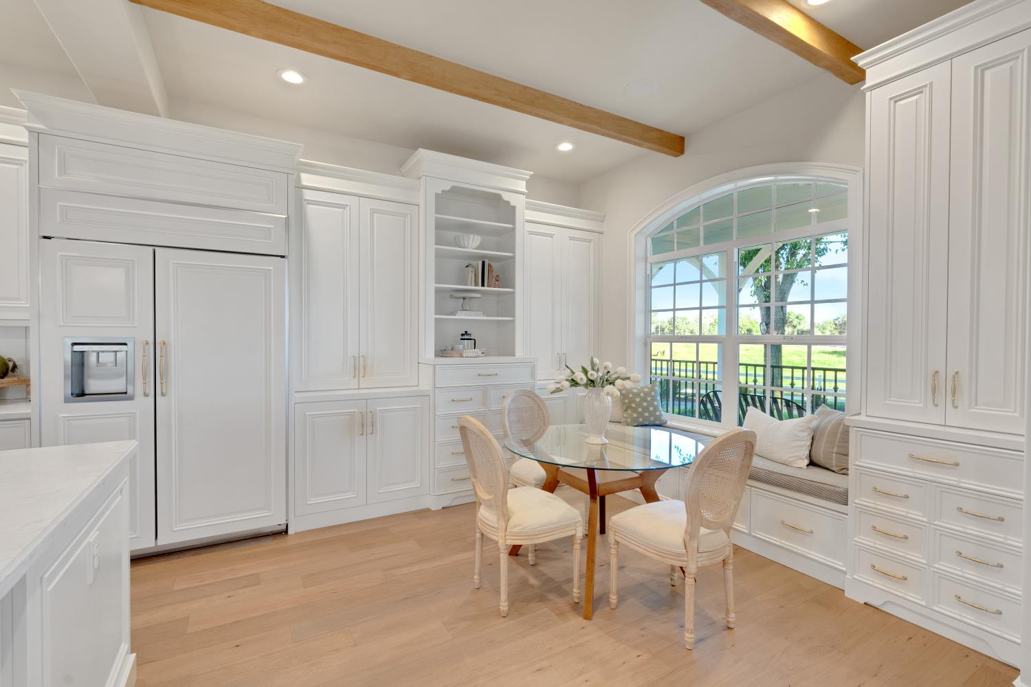 2905 Virginiatown Road Lincoln, CA 95648 - Photo 12 of 86 Bright kitchen featuring extensive white cabinetry, integrated refrigerator, wood-finish flooring, exposed ceiling beams, and a built-in window bench below an arched window