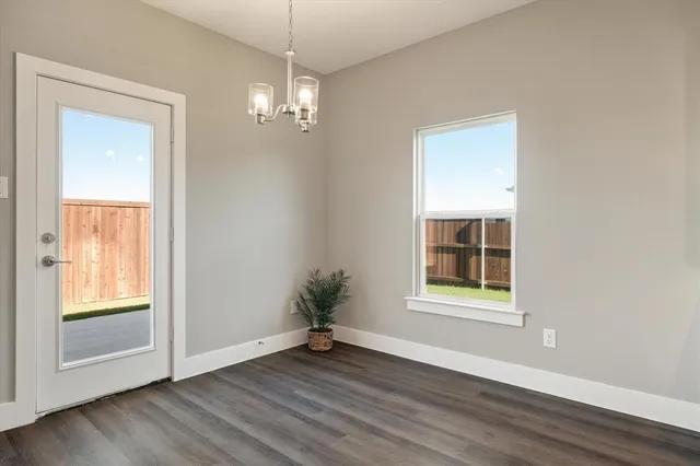 an empty room with wooden floor chandelier and windows
