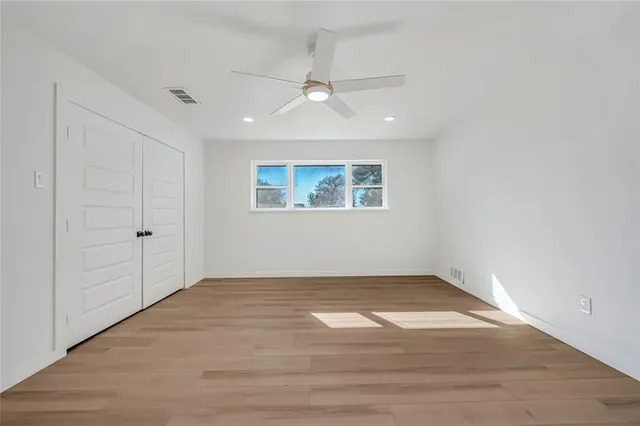 an empty room with wooden floor ceiling fan and windows