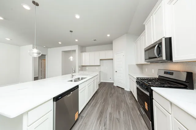 a large kitchen with stainless steel appliances a sink dishwasher a stove a microwave oven and a cabinets with wooden floor