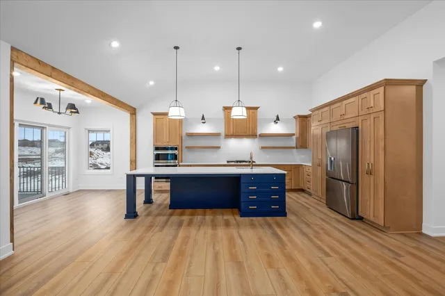 a large kitchen with stainless steel appliances granite countertop a refrigerator a oven and a wooden cabinets with wooden floor