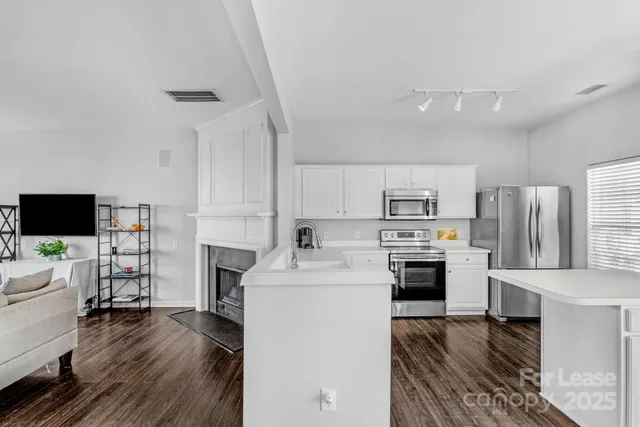 a living room with stainless steel appliances furniture a fireplace a flat screen tv and a couch