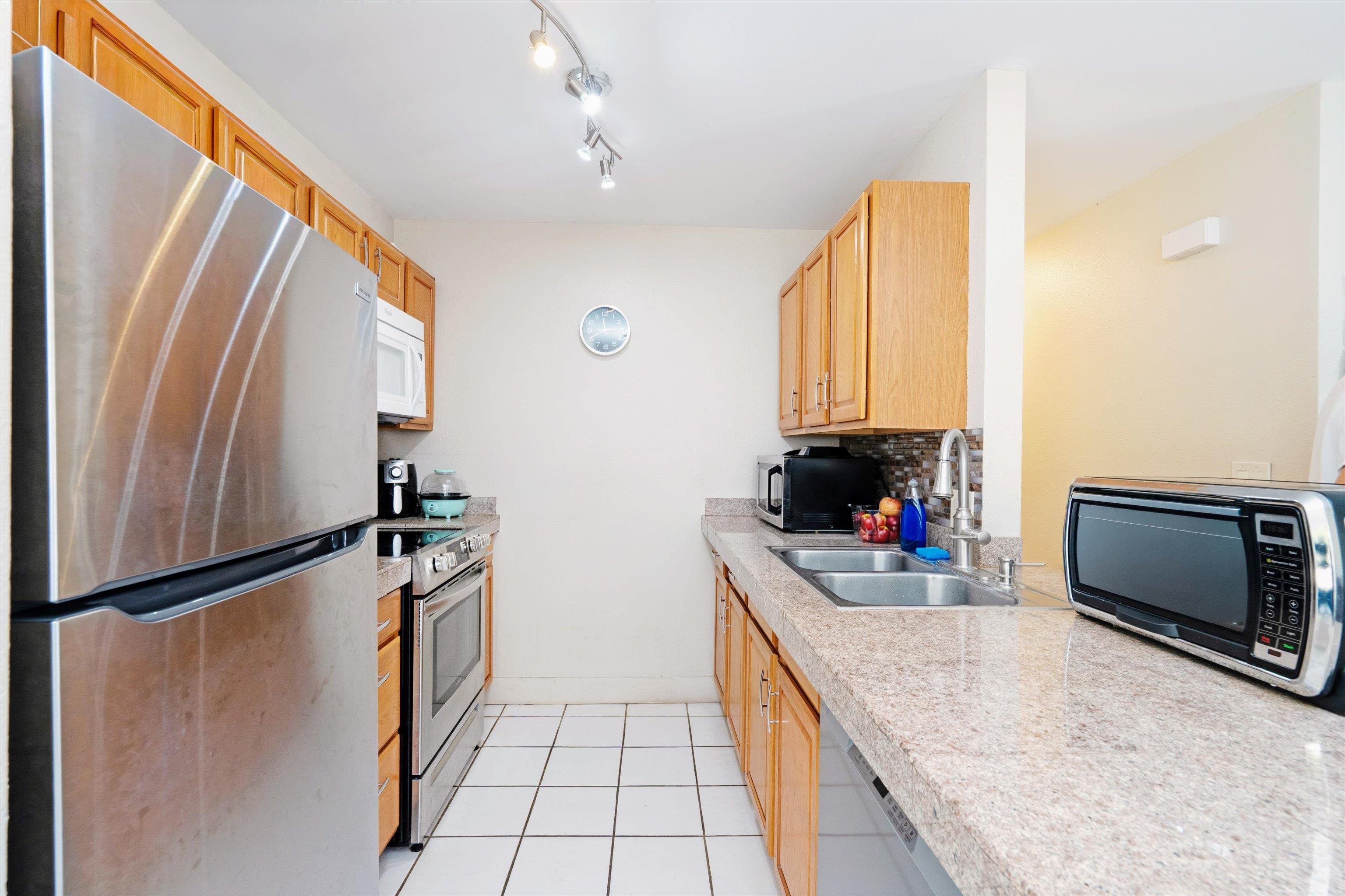 140 Uwapo Road, Unit 19105 Kihei, HI 96753 - Photo 5 of 42 a kitchen with stainless steel appliances granite countertop a refrigerator a stove and a sink with wooden floor