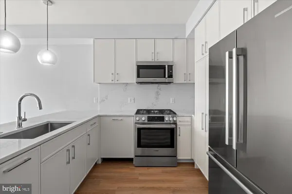a view of an empty room with wooden floor and a kitchen