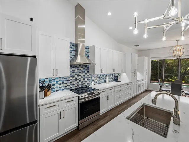 a large kitchen with stainless steel appliances kitchen island a large counter top a stove a chimney a sink and a center island