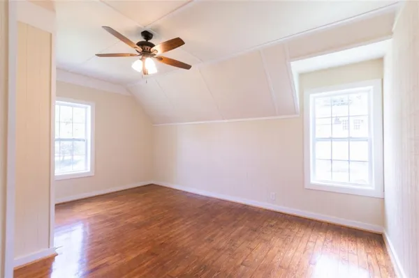 an empty room with wooden floor fan and windows