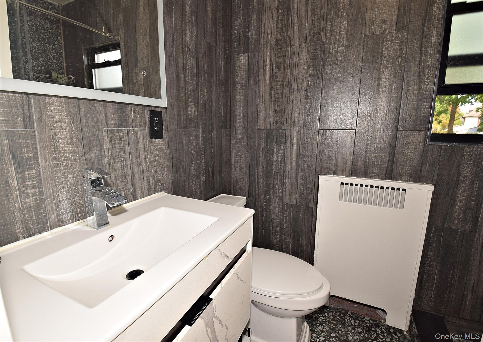 25 Old Mill Road Great Neck, NY 11023 - Photo 23 of 45 Vanity with integrated white basin, chrome faucet, and gray wood-finish wall paneling