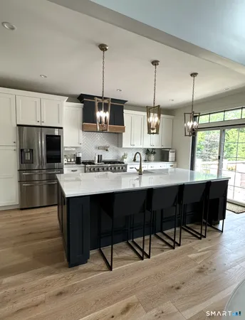 a kitchen with stainless steel appliances granite countertop a sink a stove a refrigerator cabinets and dining table with wooden floor