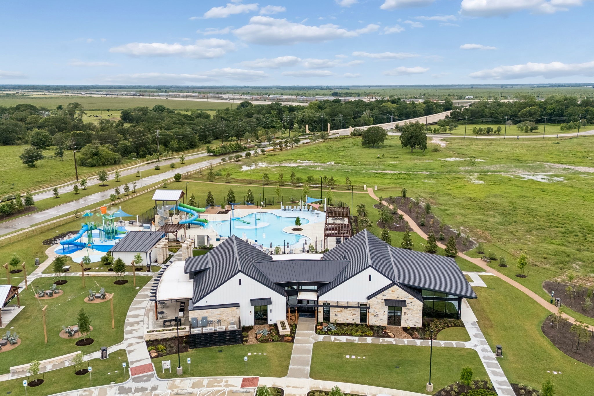 10902 Bonfire Trail Beasley, TX 77417 - Photo 30 of 36 This photo showcases a community clubhouse with a modern design, featuring a large pool area complete with water slides and splash zones. It's surrounded by expansive green spaces and walking paths, offering scenic views and ample recreational opportunities.