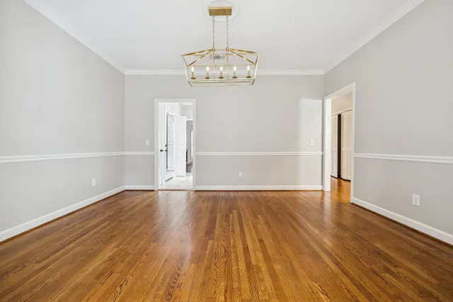 an empty room with wooden floor chandelier fan and windows