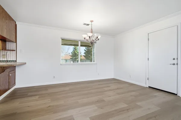 an empty room with wooden floor chandelier and windows