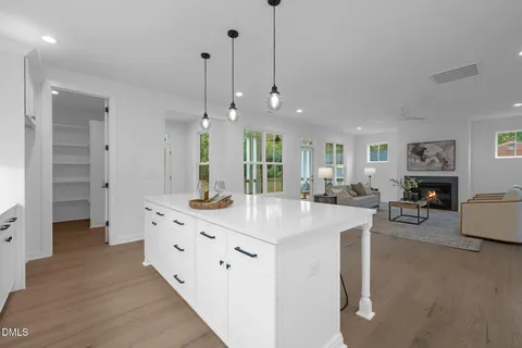 a living room with furniture white wooden floor and kitchen view
