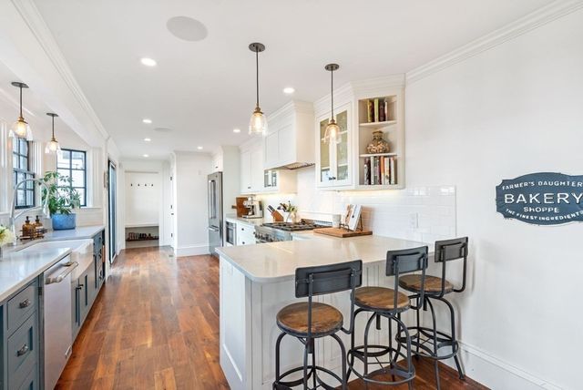 a open kitchen with stainless steel appliances granite countertop a stove top oven a sink dishwasher a dining table and chairs with wooden floor