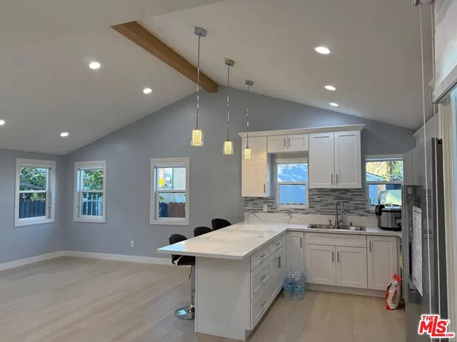 a large white kitchen with a stove a sink a refrigerator and white cabinets with wooden floor