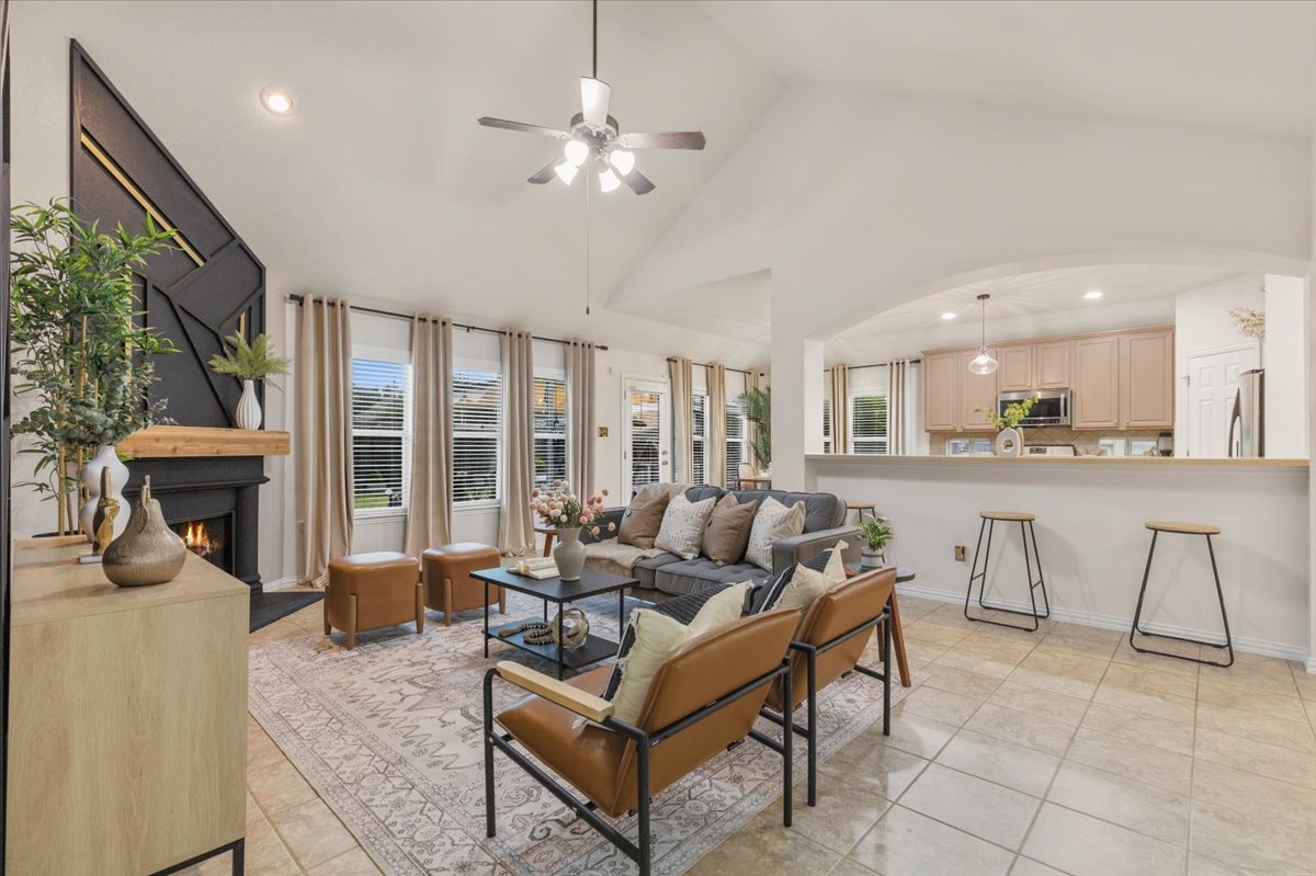 2501 Aspen Meadow Road Leander, TX 78641 - Photo 9 of 30 Spacious living area featuring a vaulted ceiling with a ceiling fan, a fireplace with a wood mantel and decorative surround, and a series of large windows