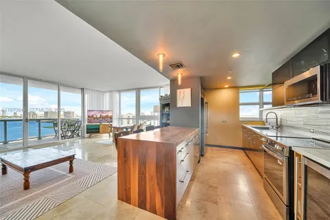 a living room with stainless steel appliances furniture a rug and a kitchen view