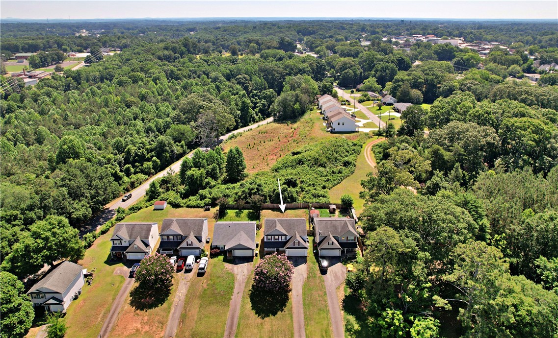 305 North Chestnut Street Seneca, SC 29678 - Photo 44 of 44 An aerial perspective showcases a residential street nestled amidst dense, verdant woodlands, with distant buildings visible on the horizon.