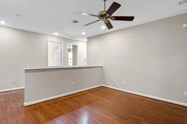 a view of an empty room with wooden floor and a ceiling fan